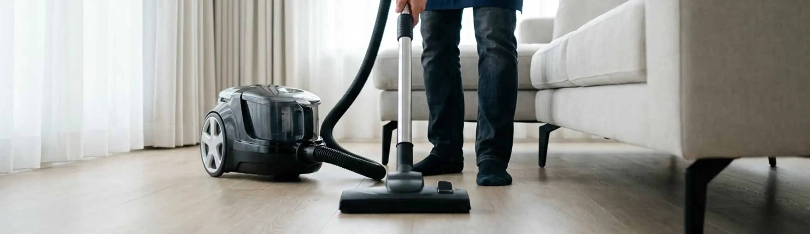 Professional house cleaner vacuuming a living room floor with a canister vacuum cleaner, Eugene, OR.
