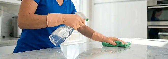 Maid service worker spraying and wiping a kitchen countertop with a microfiber cloth for sanitizing, Eugene, OR.
