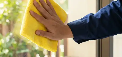 House cleaner wiping a glass window with a yellow microfiber cloth for streak-free cleaning, Eugene, OR.